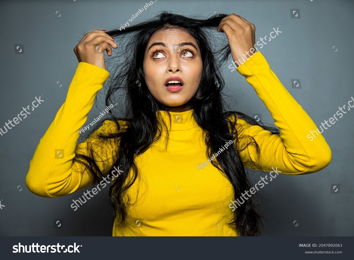 Beautiful Frustrated Indian Young Woman With Long Disheveled Hair.
Holding Messy Un-brushed Dry black Hair In Hands. Hair Damage, Health And Beauty Concept.
 #2047892063