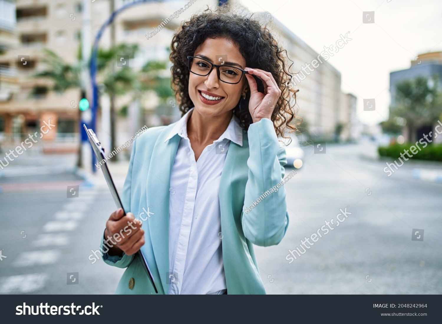 Young hispanic business woman wearing professional look smiling confident at the city holding worker clipboard #2048242964