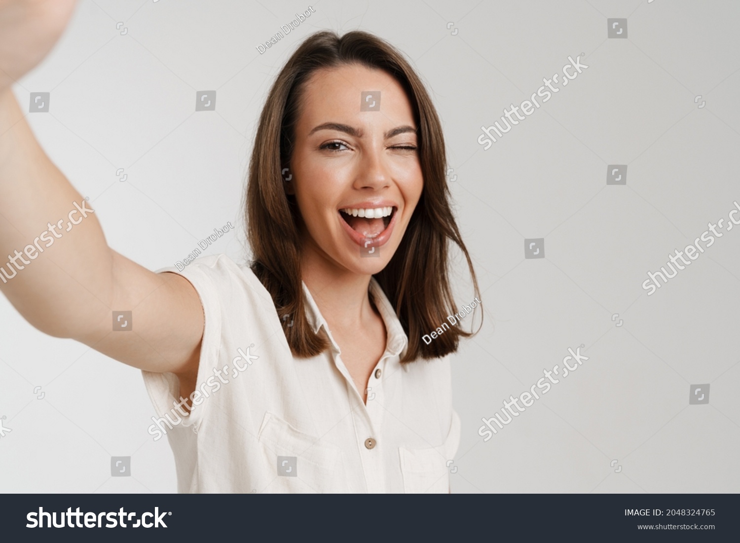 Young european woman winking while taking selfie photo isolated over white background #2048324765