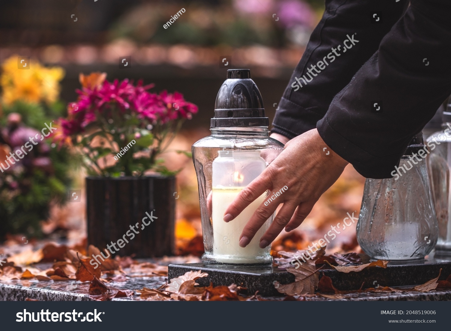Woman is putting candle lantern at grave in cemetery. Grief and paying respect for dead person #2048519006