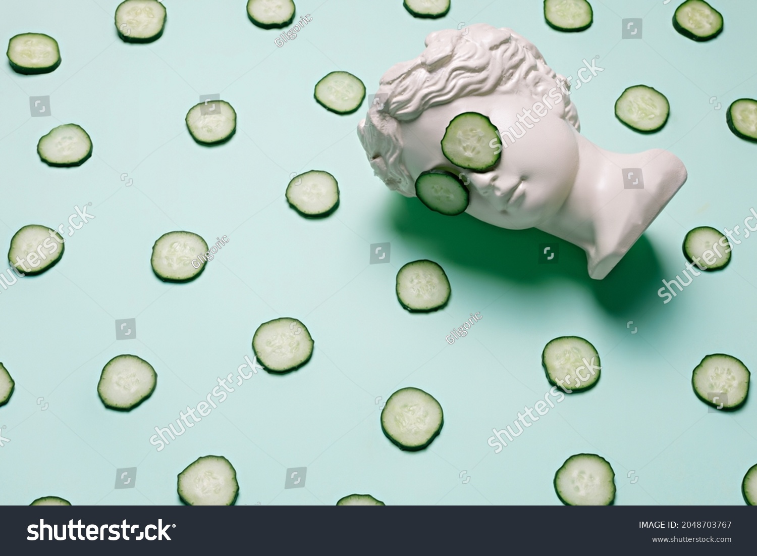 Fresh cucumber slices pattern and ancient bust with a cucumber slice mask on eyes on green background. Creative beauty concept. Spa beauty treatments at home, body care concept, organic cosmetics. #2048703767