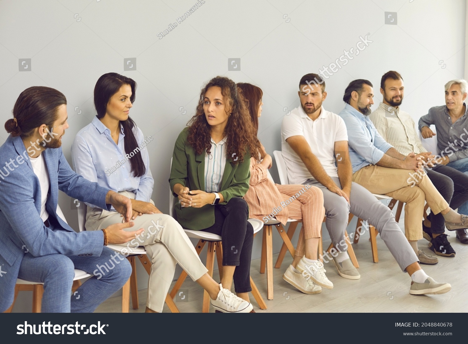 Groups of serious people of different ages talking and having discussions while sitting in queue by office wall waiting for job interview, public lecture, training session, audition or business event #2048840678