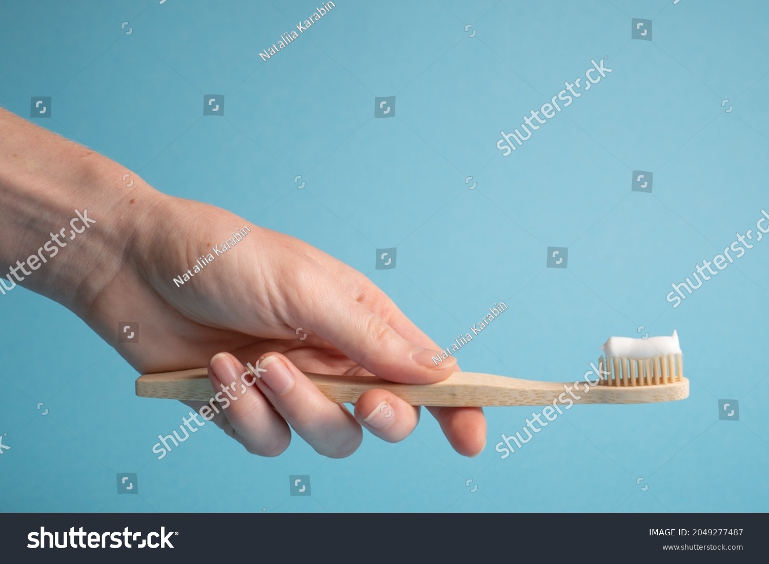 Hand holding bamboo toothbrush on blue. Holding wooden eco toothbrush. Natural toothpaste on a bamboo toothbrush #2049277487