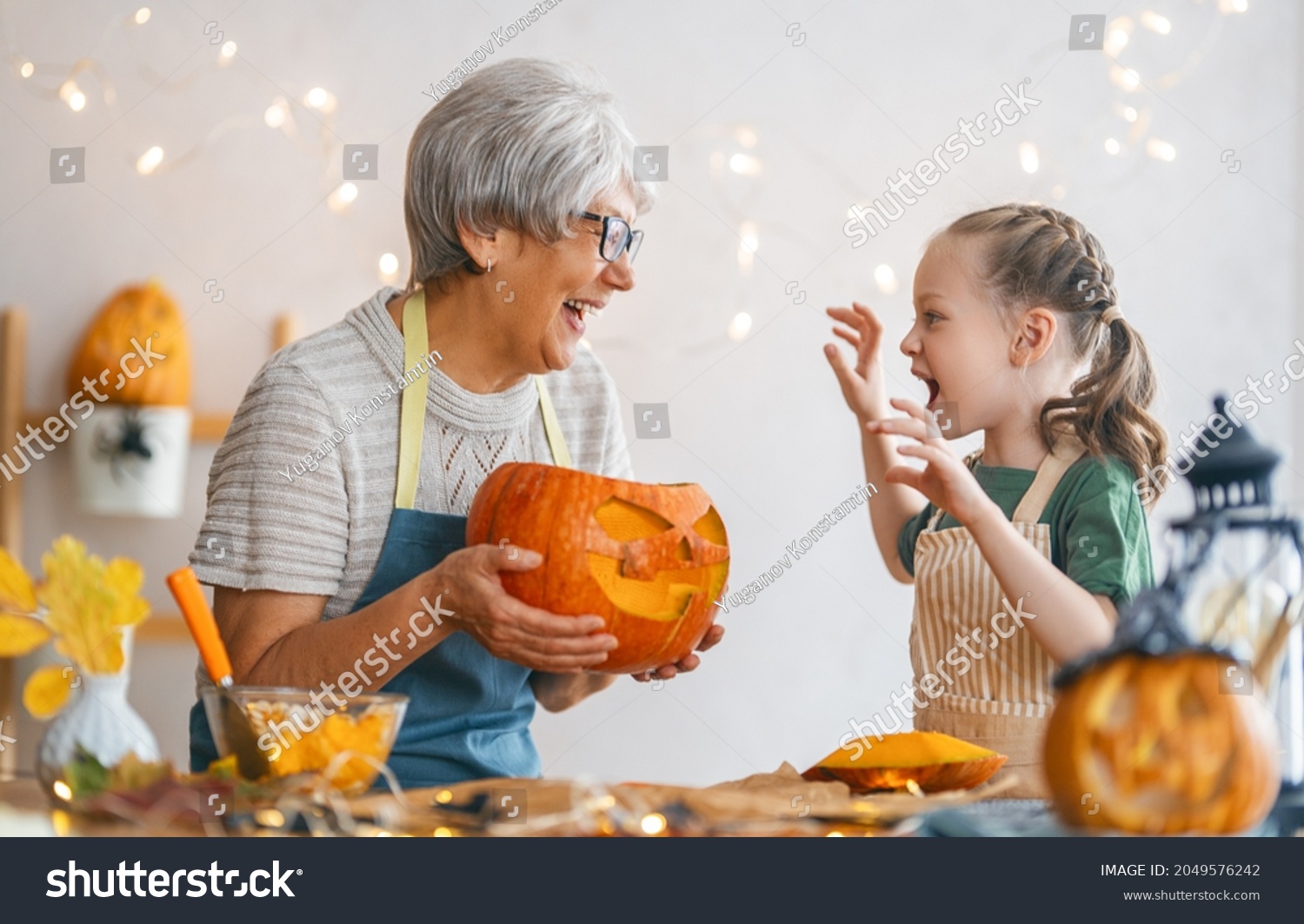 Happy family preparing for Halloween. Grandmother and granddaughter carving pumpkins at home. #2049576242