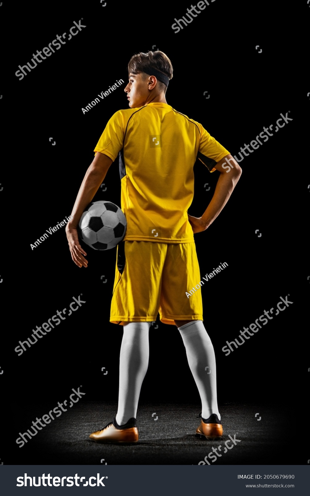 Back view full-length portrait of young handsome football player in yellow uniform isolated over black background. Concept of action, team sport game, energy, vitality. Copy space for ad. #2050679690