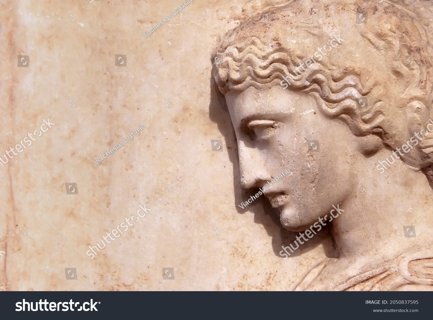 Ancient Greek relief of woman on marble wall, Greece. Beautiful stone sculpture, side view of face, art and history of old Greece. Concept of monument, culture, past civilization, antique and people. #2050837595