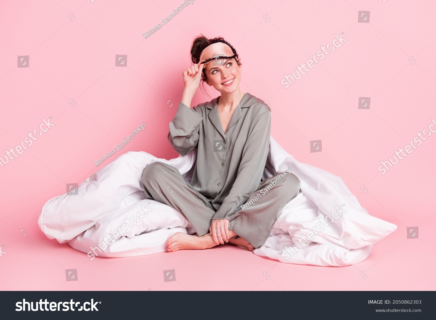 Portrait of attractive dreamy cheerful girl in pajama sitting on bed linen isolated over pink pastel color background #2050862303