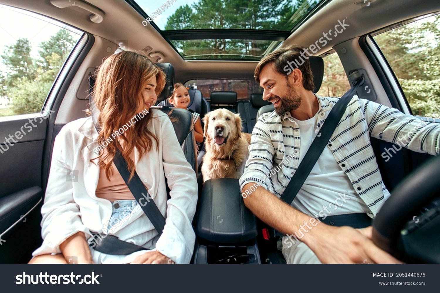 The whole family is driving for the weekend. Mom and Dad with their daughter and a Labrador dog are sitting in the car. Leisure, travel, tourism. #2051440676