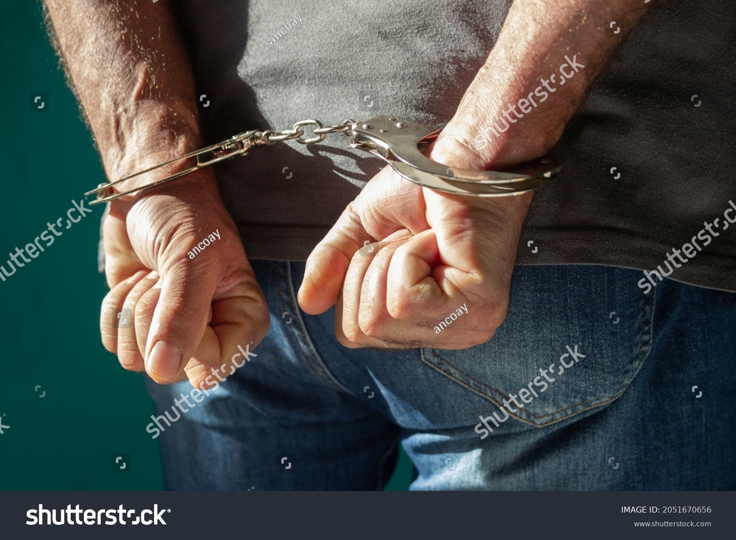 Detained man with hands behind his back. Cutaway view of a handcuffed man in jeans standing, human rights concept. #2051670656