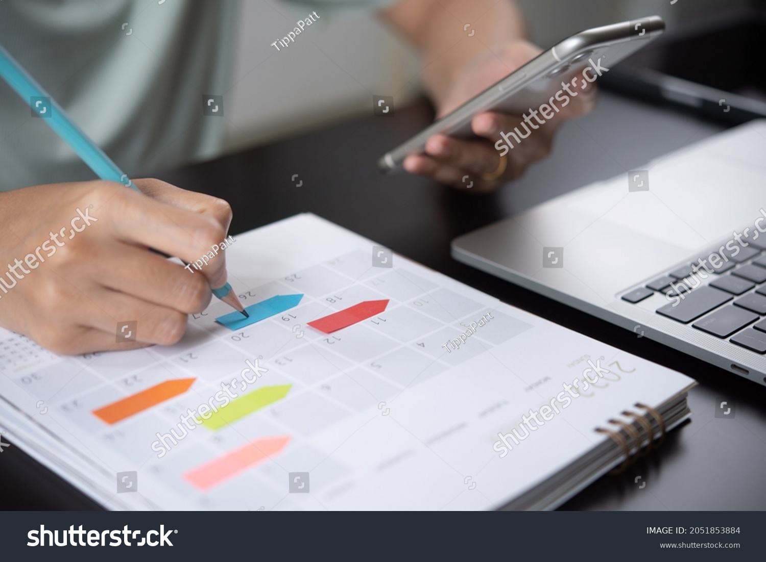 Event planner timetable agenda plan on year 2024 schedule event. Business woman checking planner on mobile phone, taking note on calendar desk on office table. Calendar event plan, work planning #2051853884