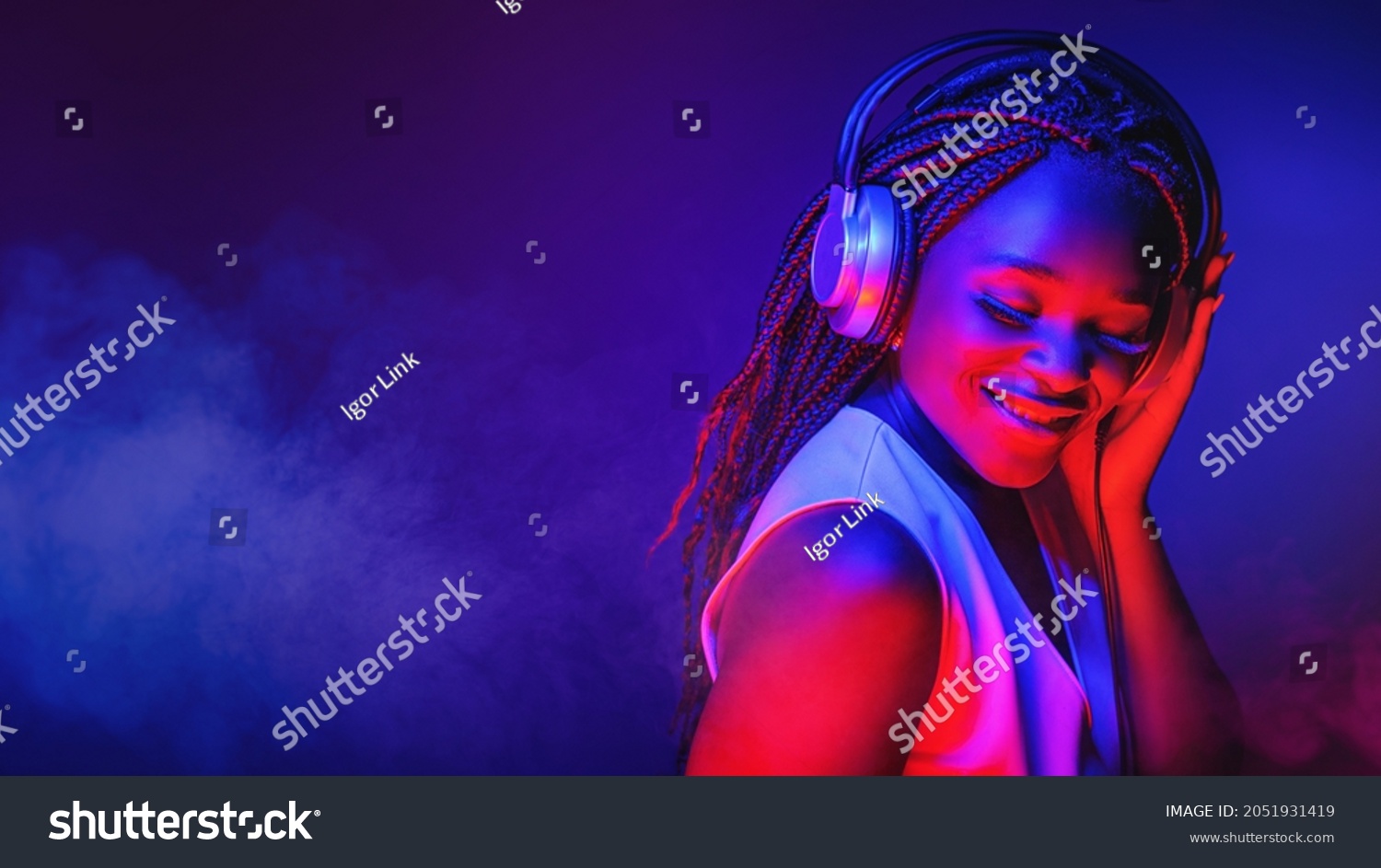Stylish fashion african american teenager model wearing headphones listening dj music dancing in purple neon lights. Young teen girl enjoy cool music #2051931419