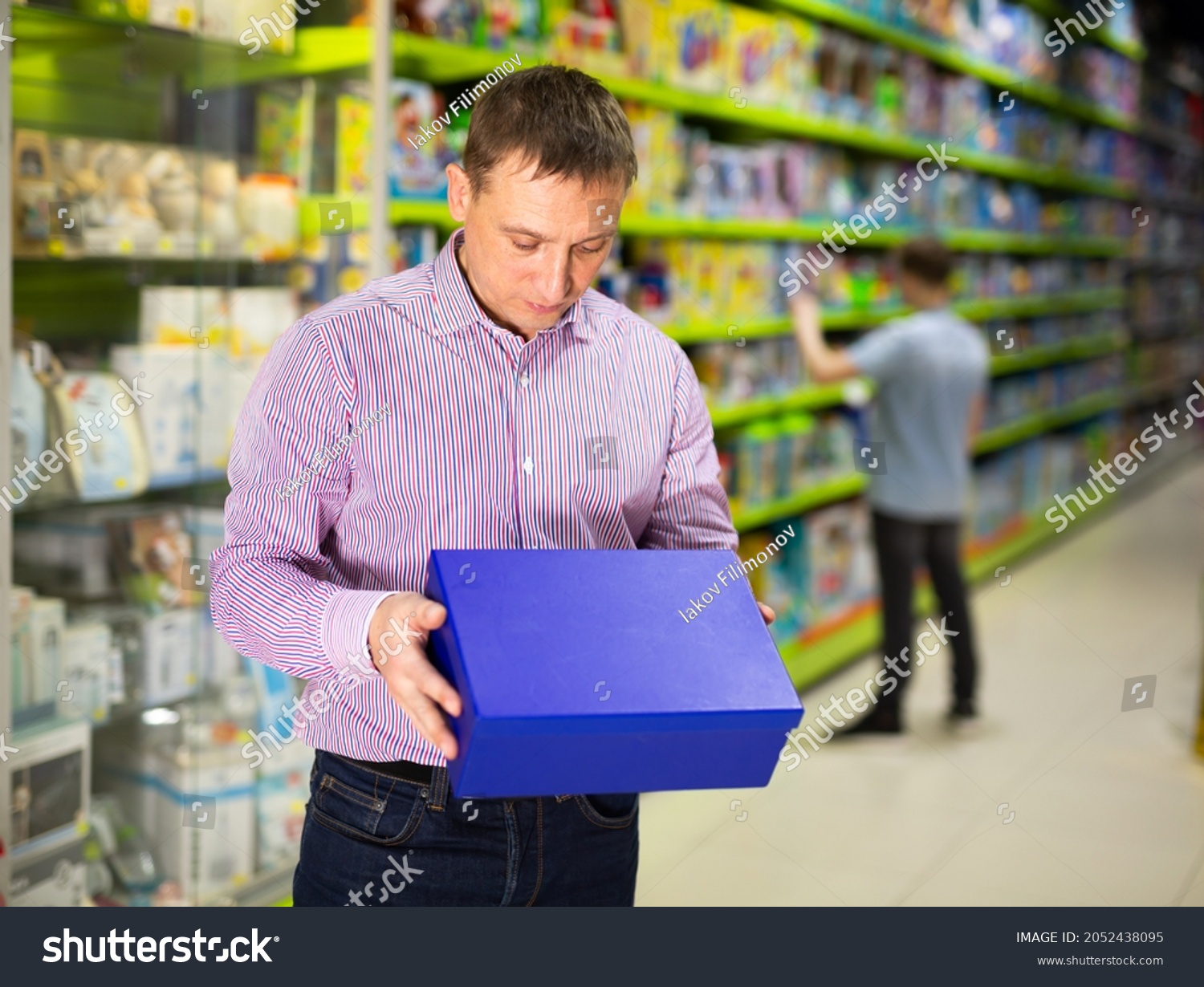 Caring father visiting toy store in search of new playthings for his child, looking narrowly at carton box #2052438095
