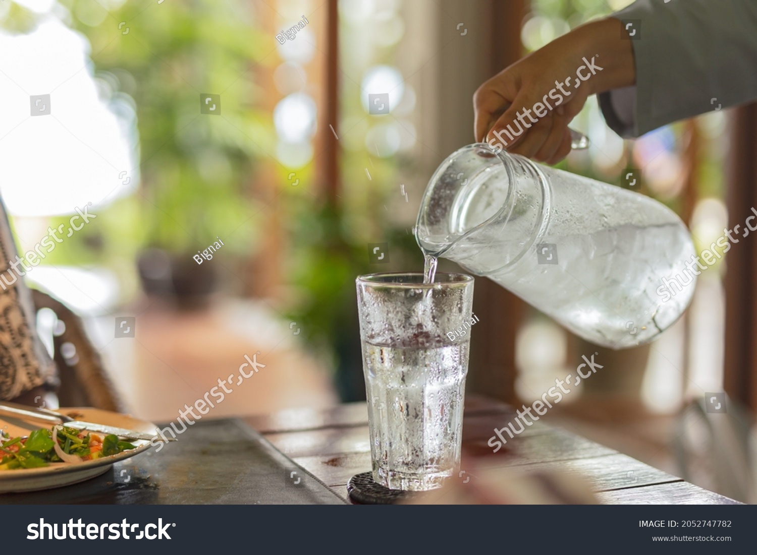 Waiter hand pouring water with ice into glasses on table #2052747782