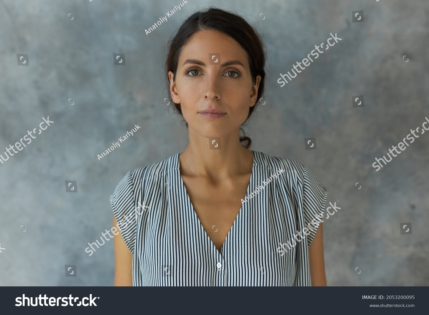 Horizontal indoor portrait of charming young lady posing for ID or passport photo, having calm face expression, looking straight at camera without smile, standing against textured studio wall #2053200095