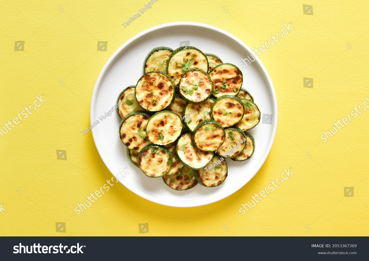 Roasted zucchini on plate over yellow background. Top view, flat lay #2053367369