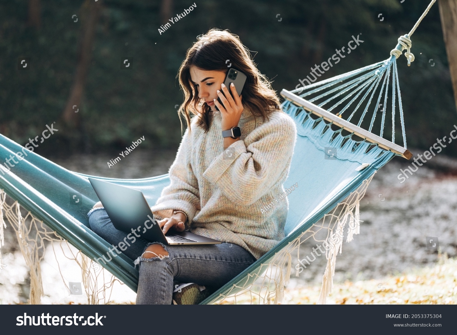 Beautiful smiling girl working with MacBook Pro in the park on a hammock #2053375304