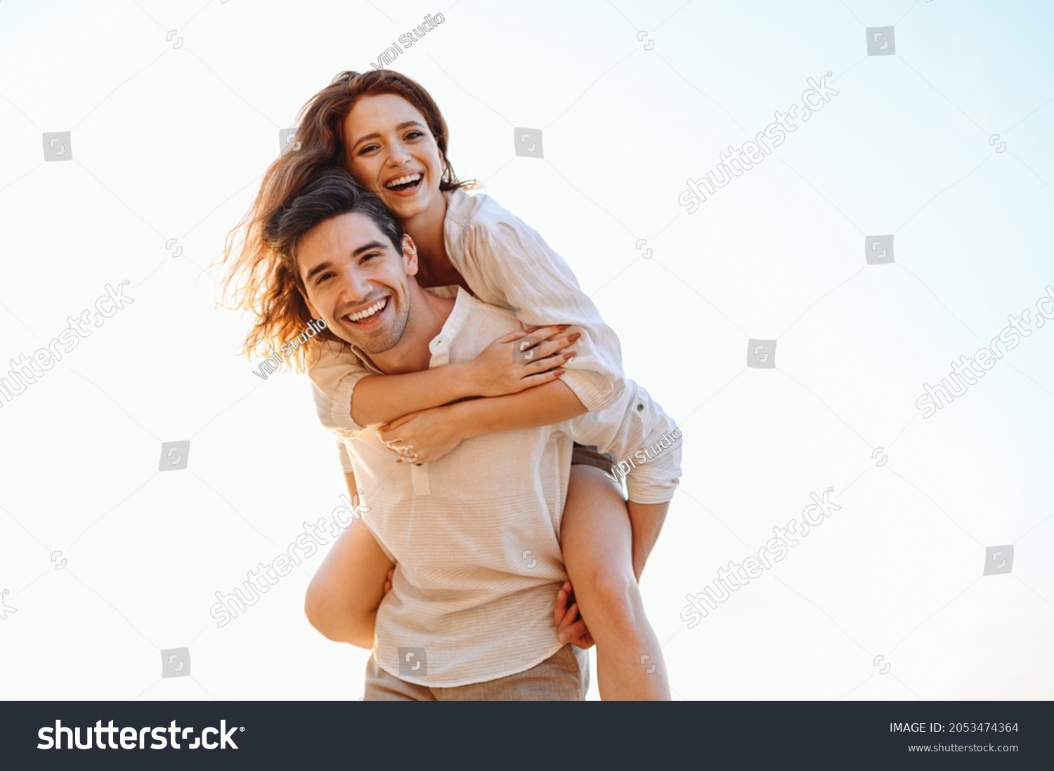 Young playful fun happy enamored smiling couple two friends family man woman in casual clothes boyfriend give piggyback ride to joyful girlfriend sit on back look aside on light white sky background #2053474364