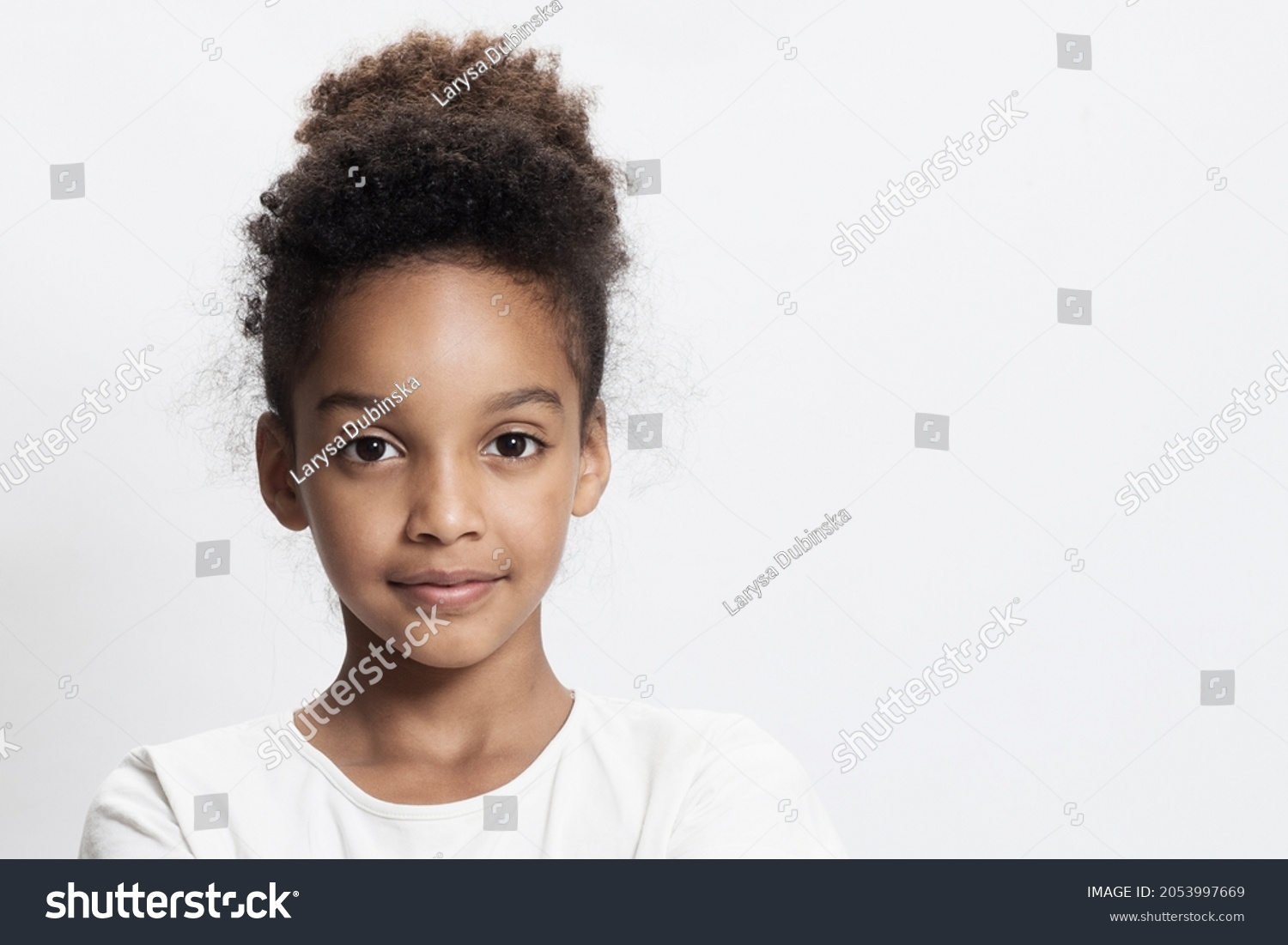 Portrait of a beautiful mixed race kid on white studio background. Beautiful young girl with afro hair. Child looks to the camera. Concept of childhood, cute schoolgirl 9-10 years old. Copy space.  #2053997669