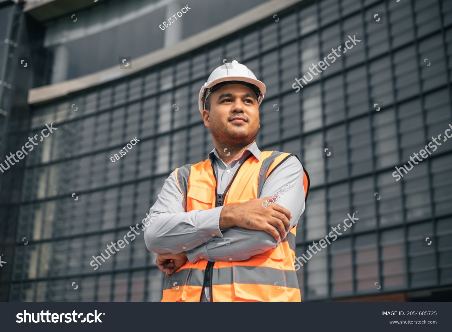 Asian engineer handsome man or architect looking forward with white safety helmet in construction site. Standing at modern building construction. Worker asian man working project building #2054685725
