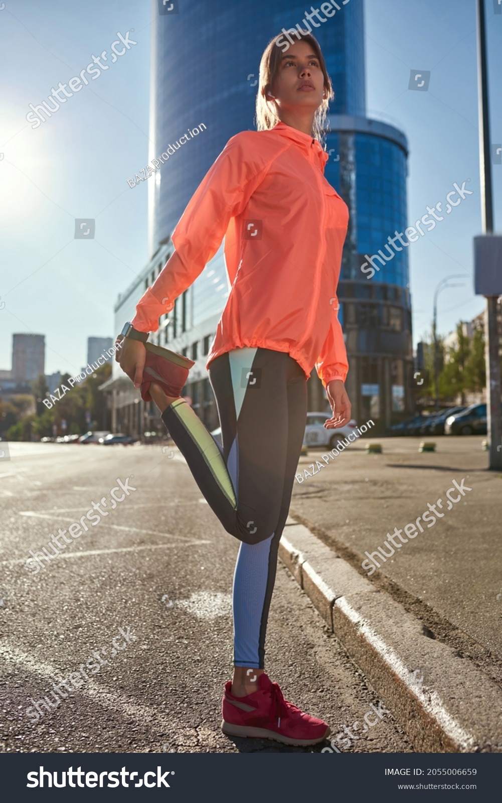 Low angle vertical narrow shot of active millennial girl in sportswear stretch work out train outdoors. Sporty young Caucasian woman do warmup running jogging in street. Sport, fitness concept. #2055006659