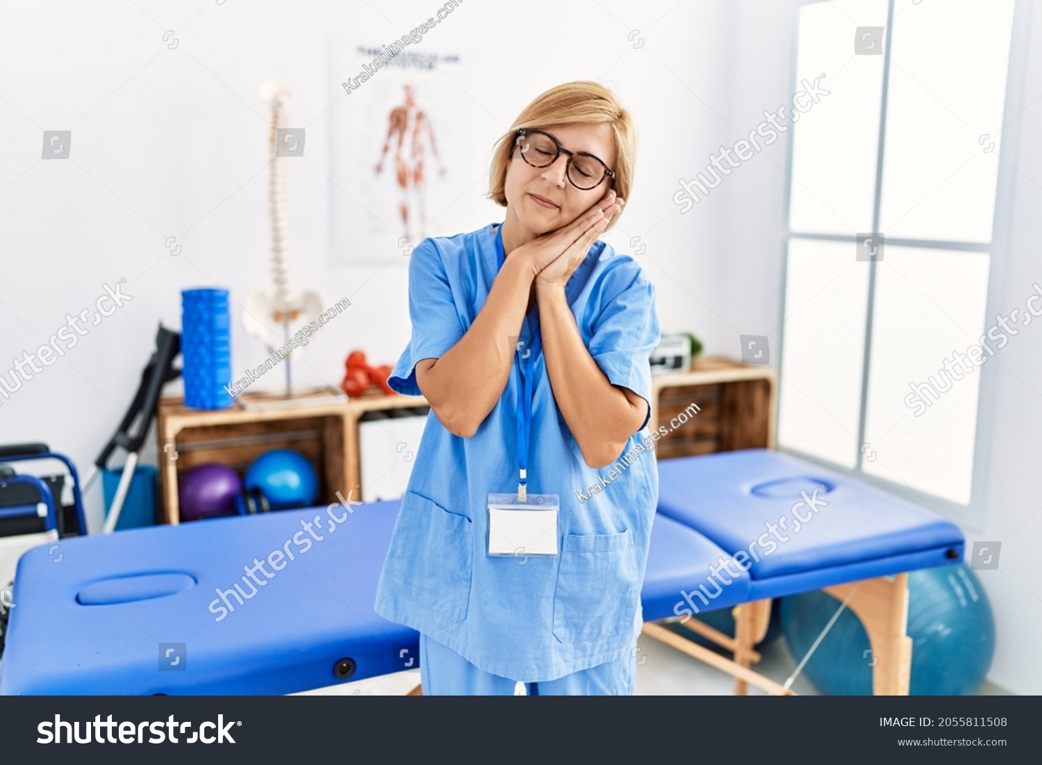 Middle age blonde woman working at pain recovery clinic sleeping tired dreaming and posing with hands together while smiling with closed eyes.  #2055811508