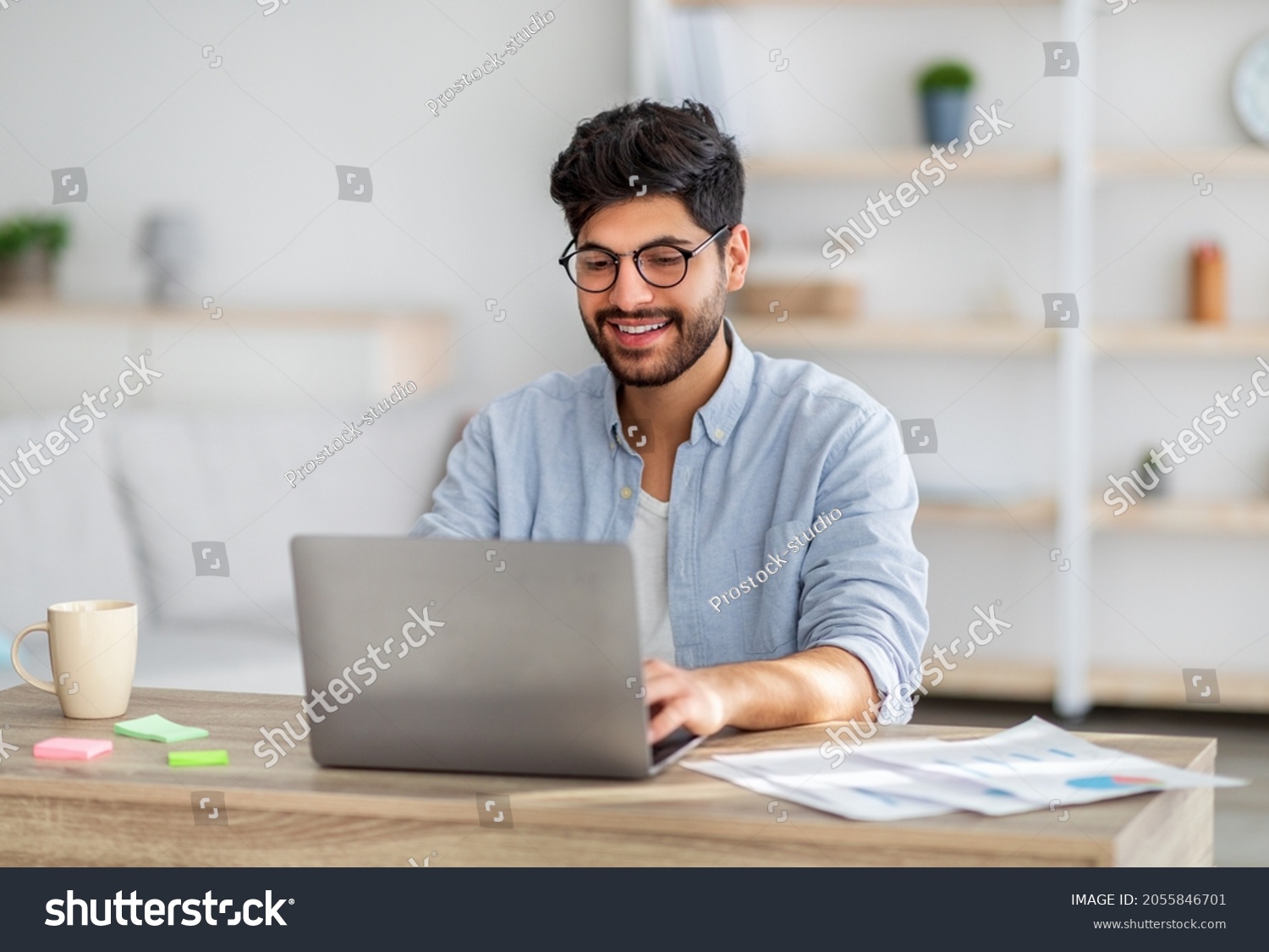 Portrait of happy arab freelancer man sitting at desk with laptop computer at home office, looking and smiling at screen, copy space. Young entrepreneur guy enjoying remote work #2055846701