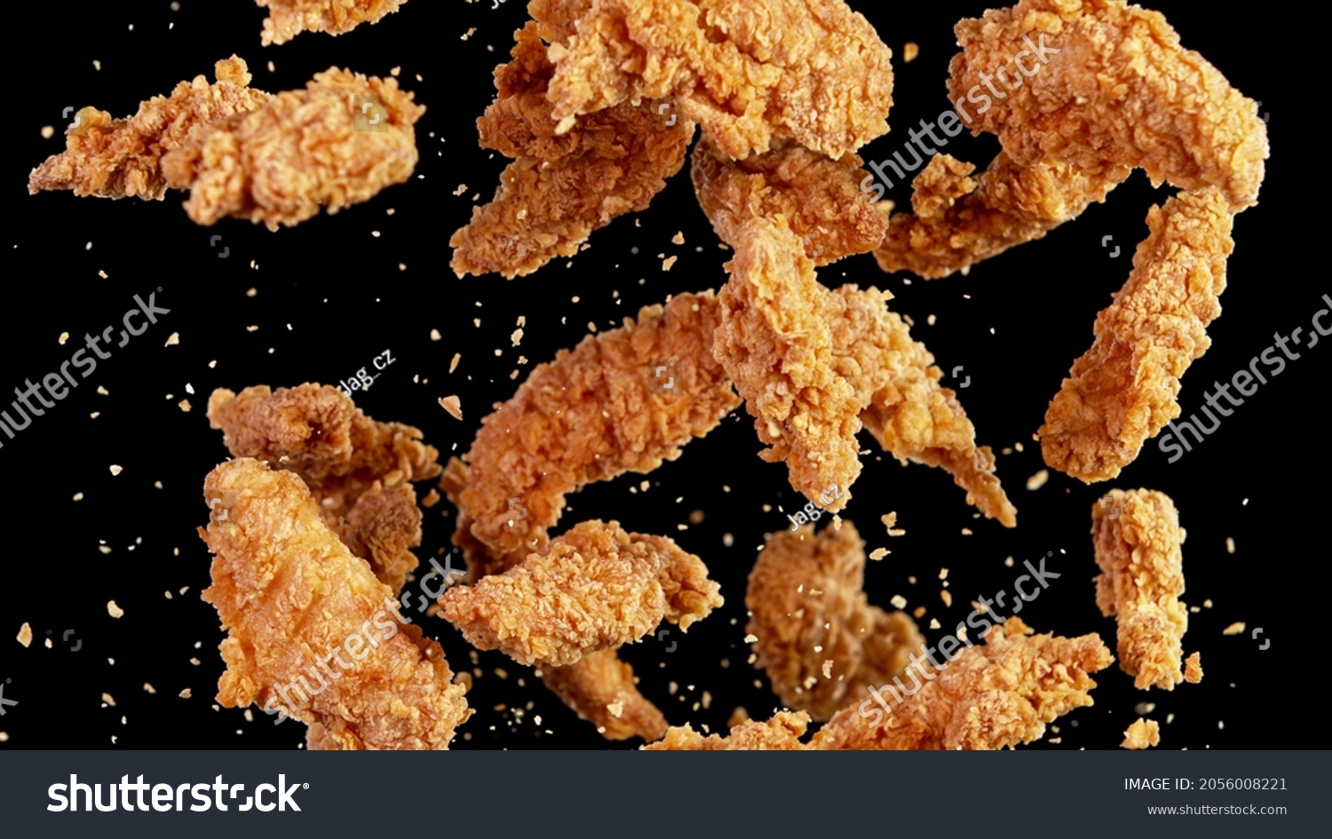 Freeze motion of flying pieces of fried chicken pieces on black background. Concept of levitating food. #2056008221