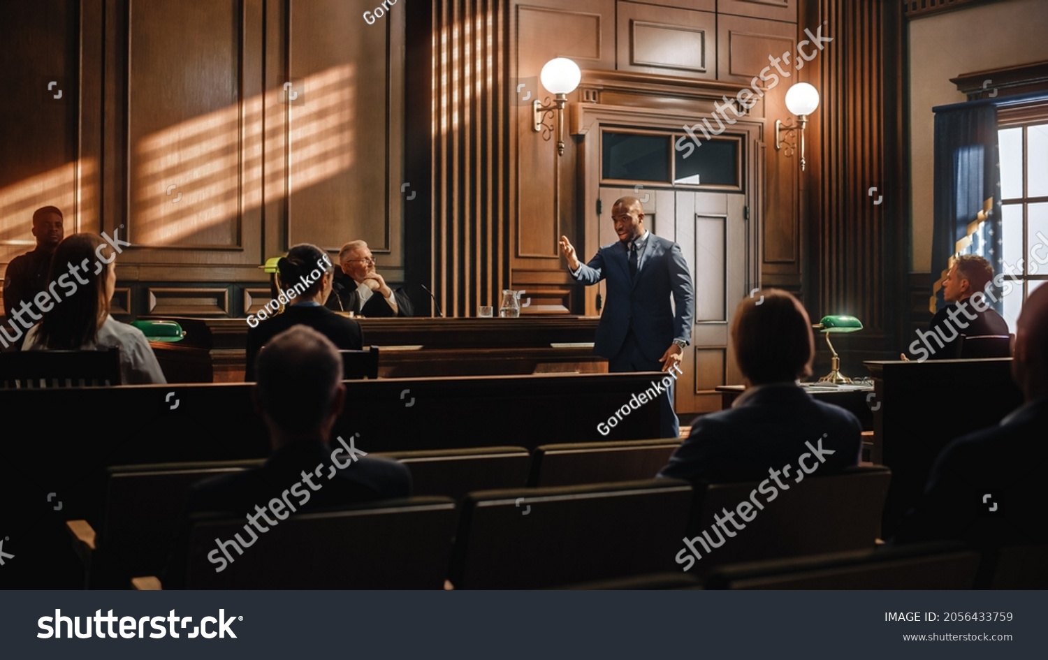 Court of Justice and Law Trial: Male Public Defender Presenting Case, Making Passionate Speech to Judge, Jury. African American Attorney Lawyer Protecting Client's Innocents with Supporting Argument. #2056433759