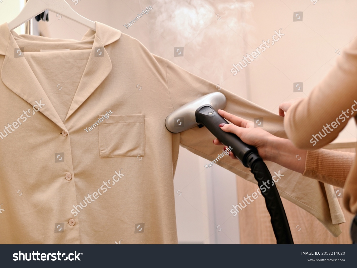 Woman using steaming iron to ironing shirt in laundry room. Girl doing stream vapor iron for press clothes in hand #2057214620