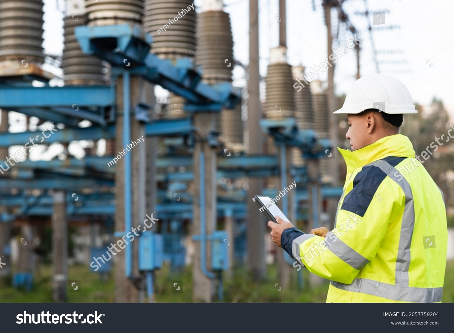 Energy business technology industry concept. Electrical engineer studying reading on tablet. Electrical worker engineer working with digital tablet near tower with electricity #2057759204