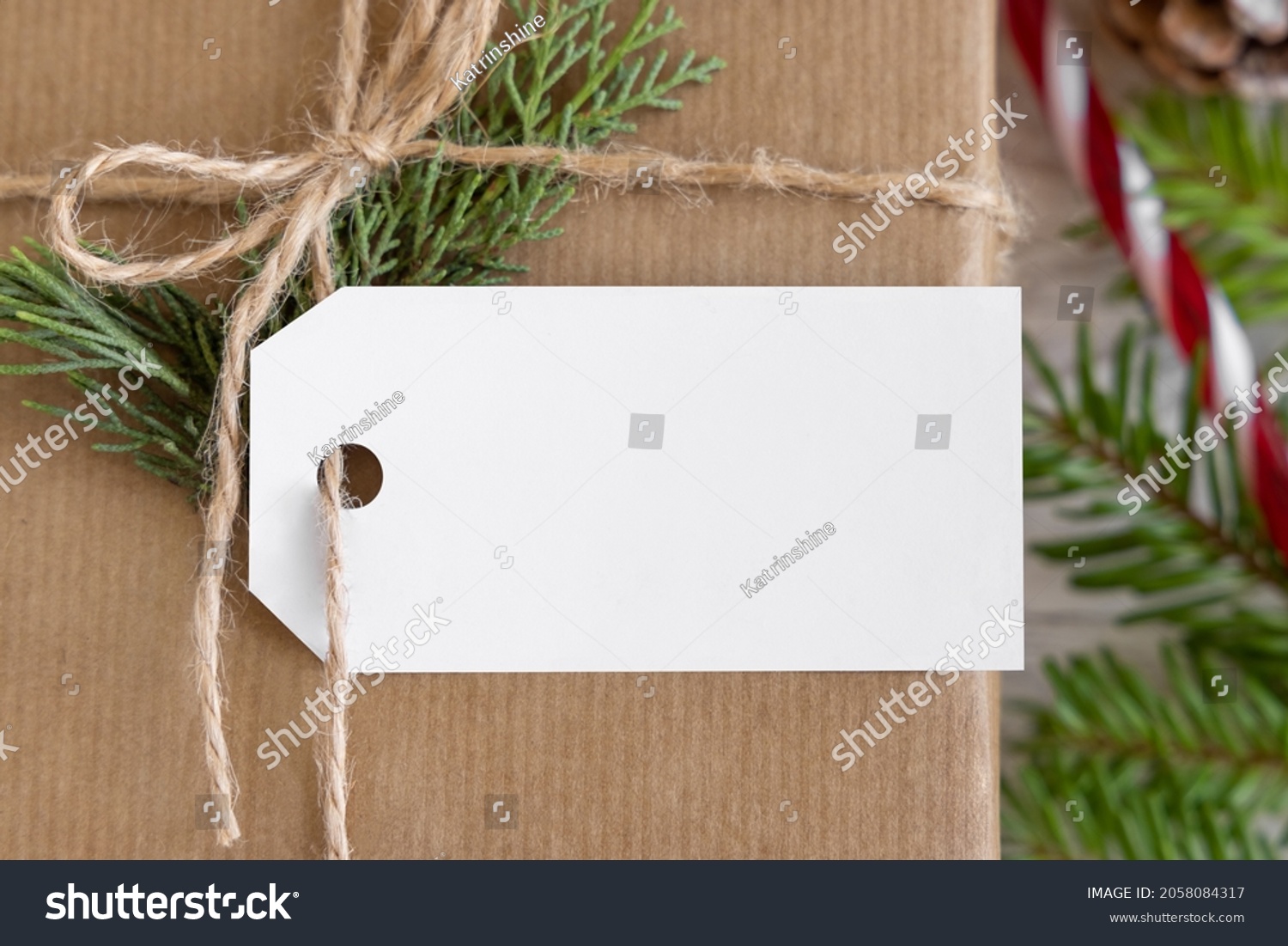 Christmas wrapped present with paper gift tag with fir tree branches, pine cones and holiday decorations close up. Rustic winter composition with blank Gift tag Mockup, copy space, flat lay #2058084317