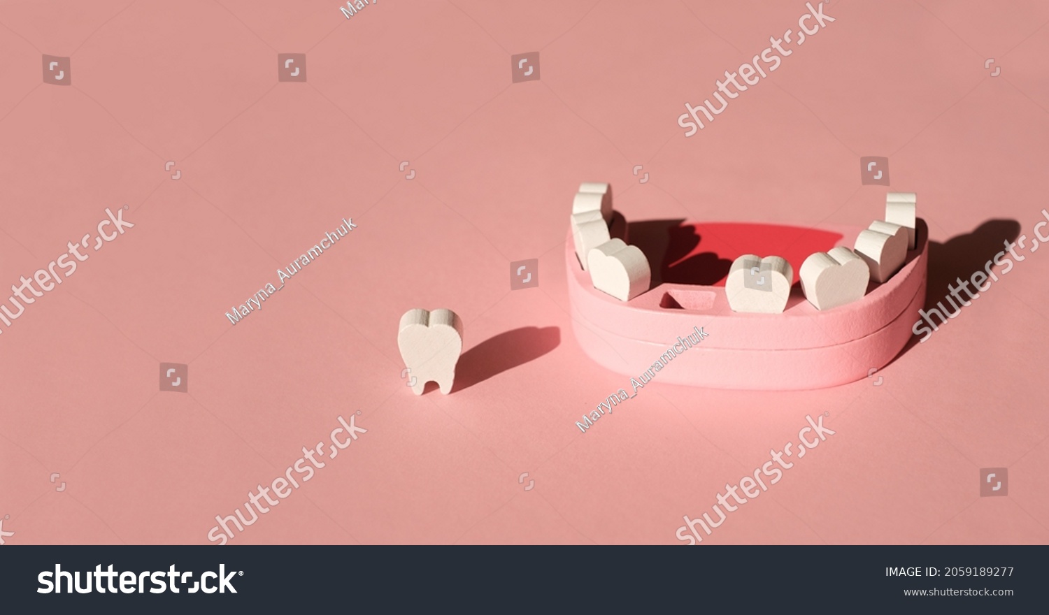 Wooden model toy of a human jaw with a missing tooth on a pink studio background. The problem of tooth loss. Baby milk teeth. Banner. Copy space.  #2059189277