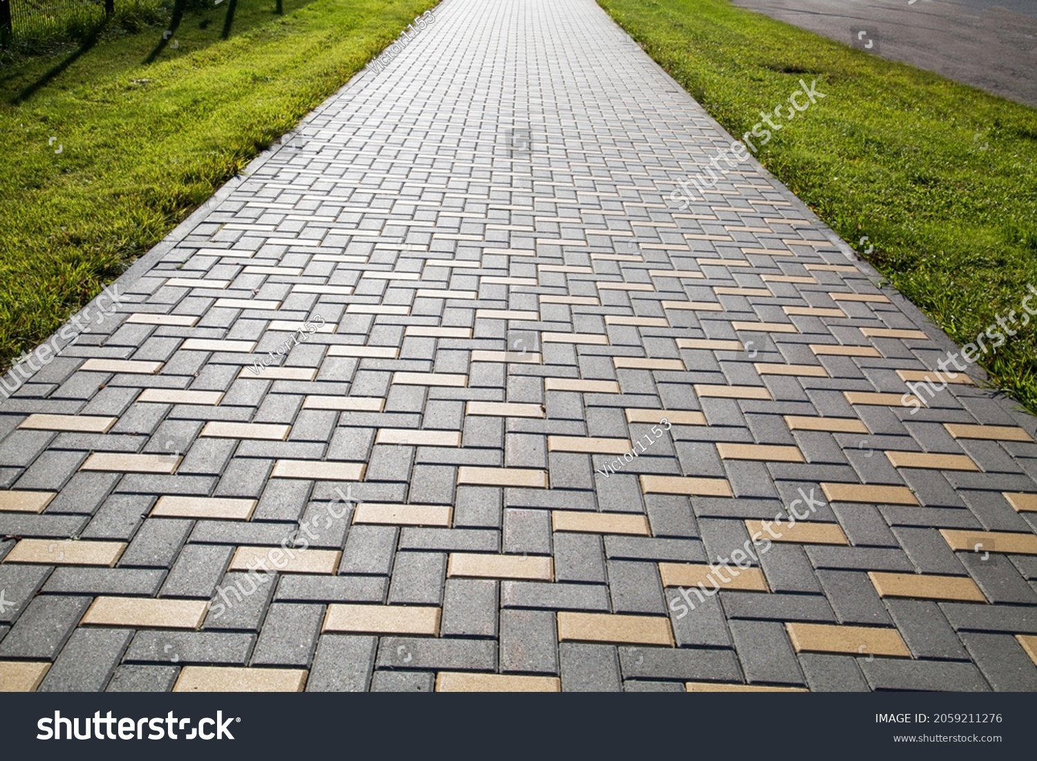 A sidewalk made of rectangular artificial stone extending into the distance in yellow and gray with a green lawn, texture backgrounds for graphic design. Abstract wallpaper. #2059211276