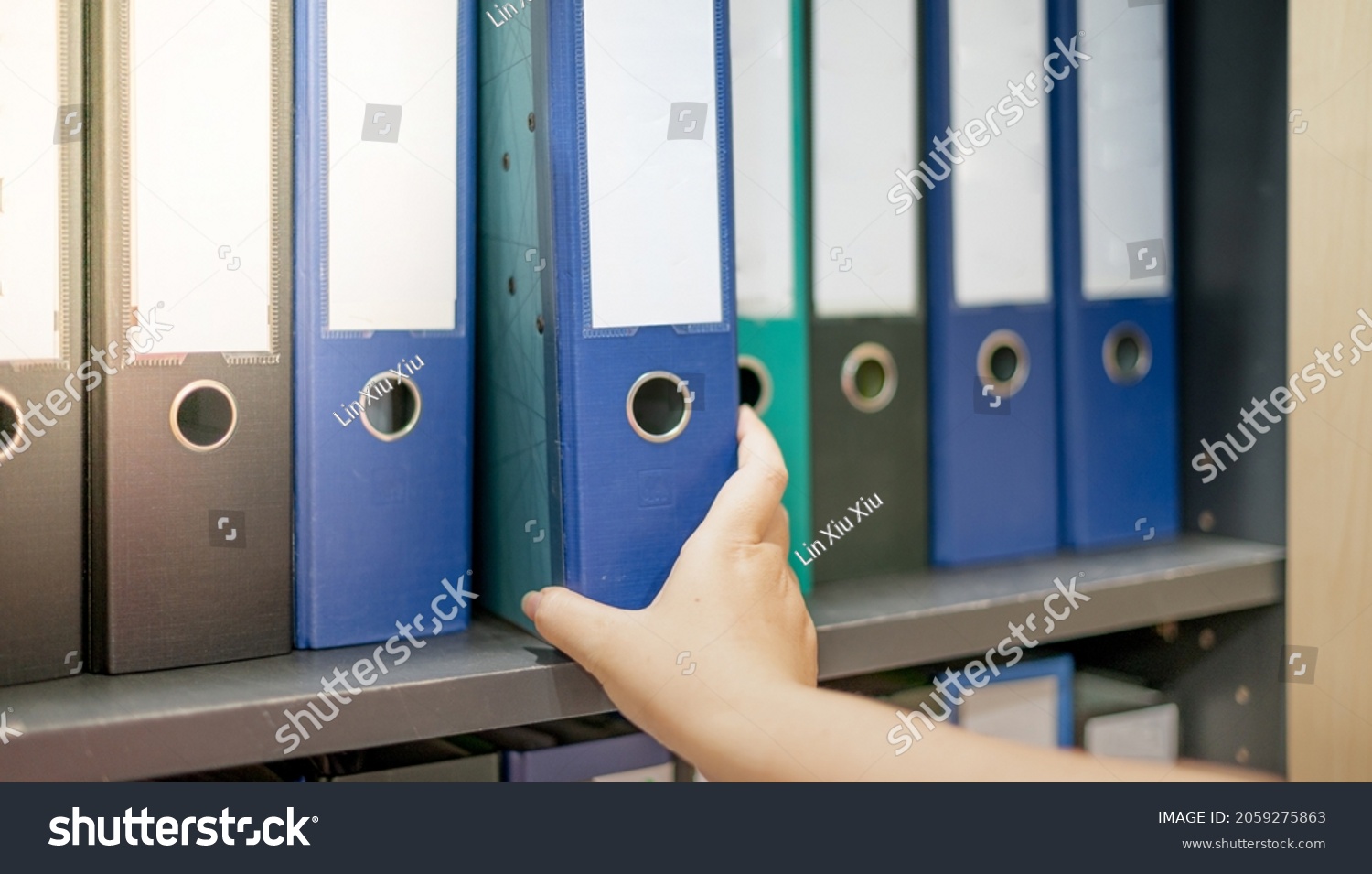 Female hand holding a binder of documents on the row of file folders that nicely management system on the office's shelves. #2059275863
