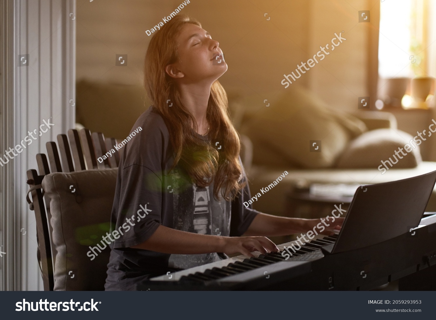 A young woman playing the piano.Close-up of a beautiful blonde girl with reddish-brown hair playing the piano creative, performance, musical concept, she wearing a T-shirt and playing a black piano. #2059293953