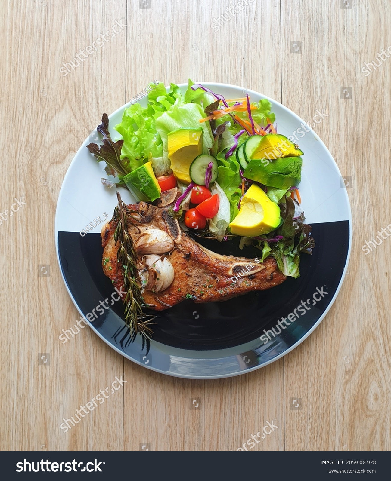 Grilled pork chop steak with salad on the black and white plate. Wooden table. Keto, ketogenic, Atkins diet recipe. Low carb, high fat. Avocado is good fat. Fresh vegetables. Diabetes patients' food. #2059384928