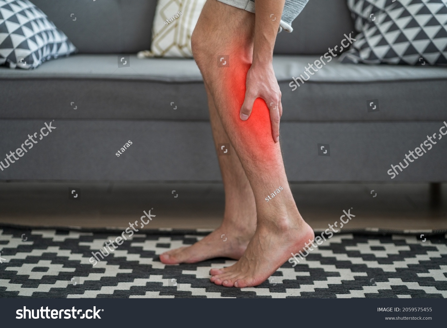 The man's calf muscle cramped, massage of male leg at home, painful area highlighted in red #2059575455