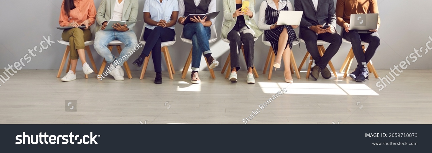 Diverse people in smart casual clothes holding paper documents, CVs, resumes, laptops and cellphones waiting in line for job interviews or business appointments in recruitment agency, legs low section #2059718873