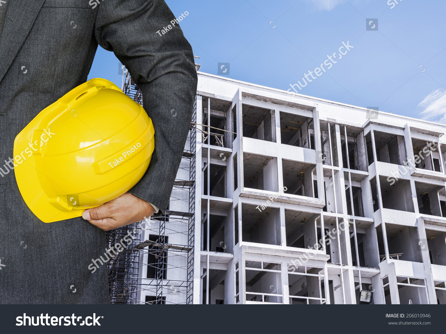 Engineer hand holding yellow helmet against the background of building under construction  #206010946