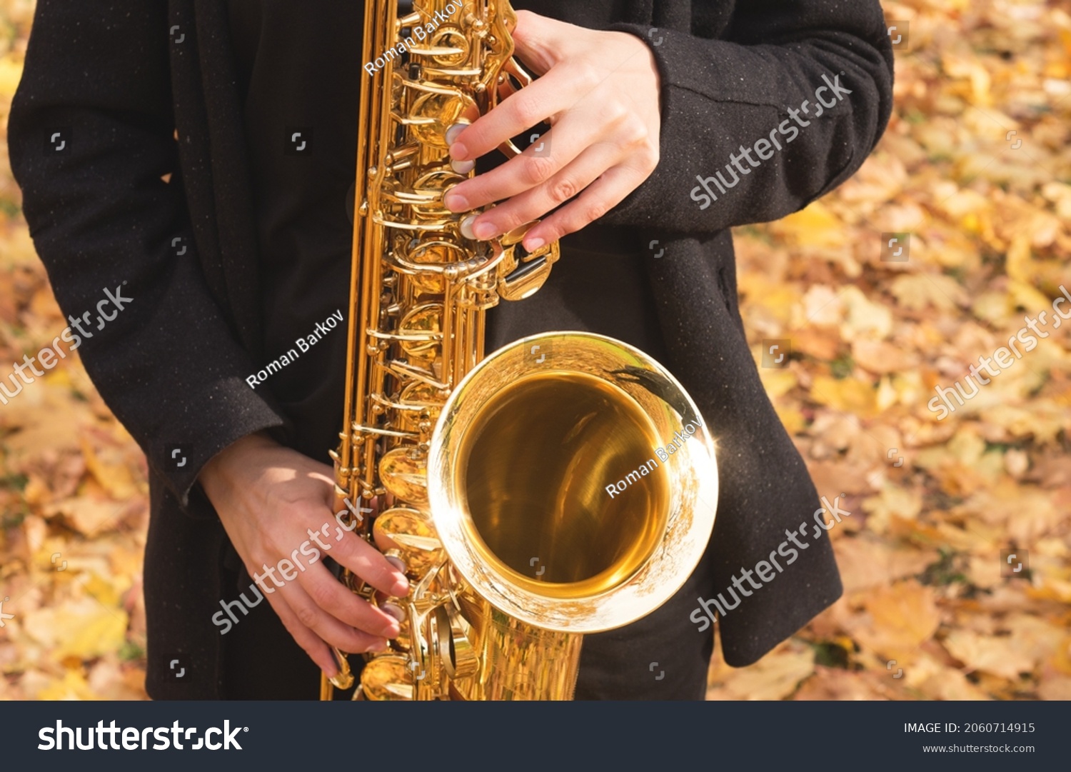The girl musician plays the saxophone. Close-up of a golden saxophone on a background of yellow leaves. #2060714915