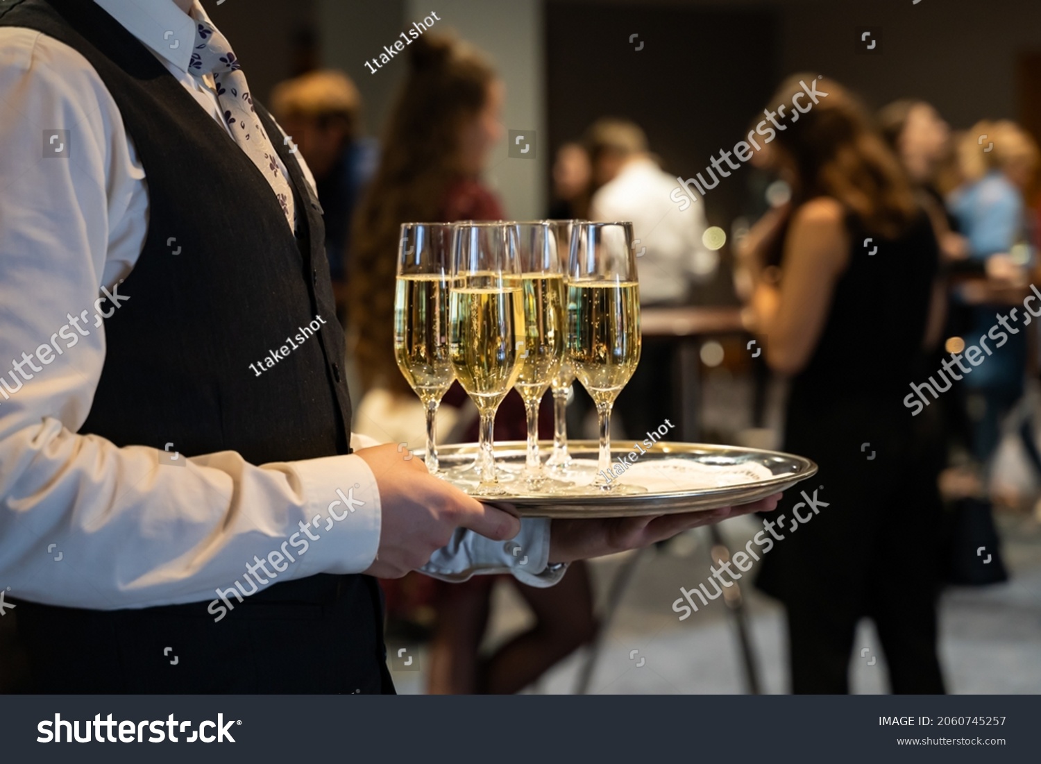 A waiter is holding a plate with sparkling wine to welcome people at an event. Glasses with champagne to toast. Drinks at a luxury party in a hotel. #2060745257