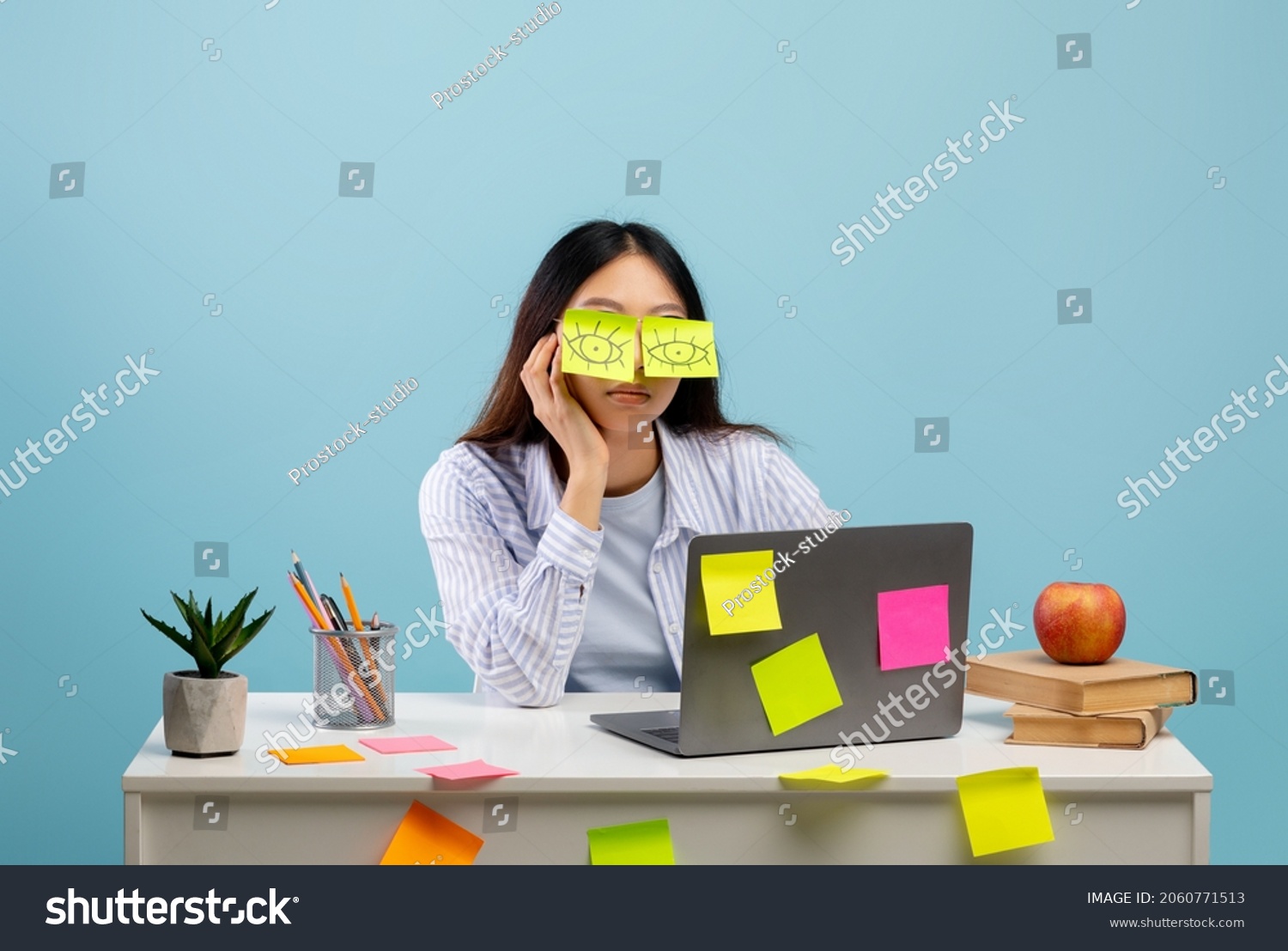 A lot of work concept. Tired asian female student sleeping with stickers on eyes, sitting at table over blue studio background. Distracted woman at home office #2060771513