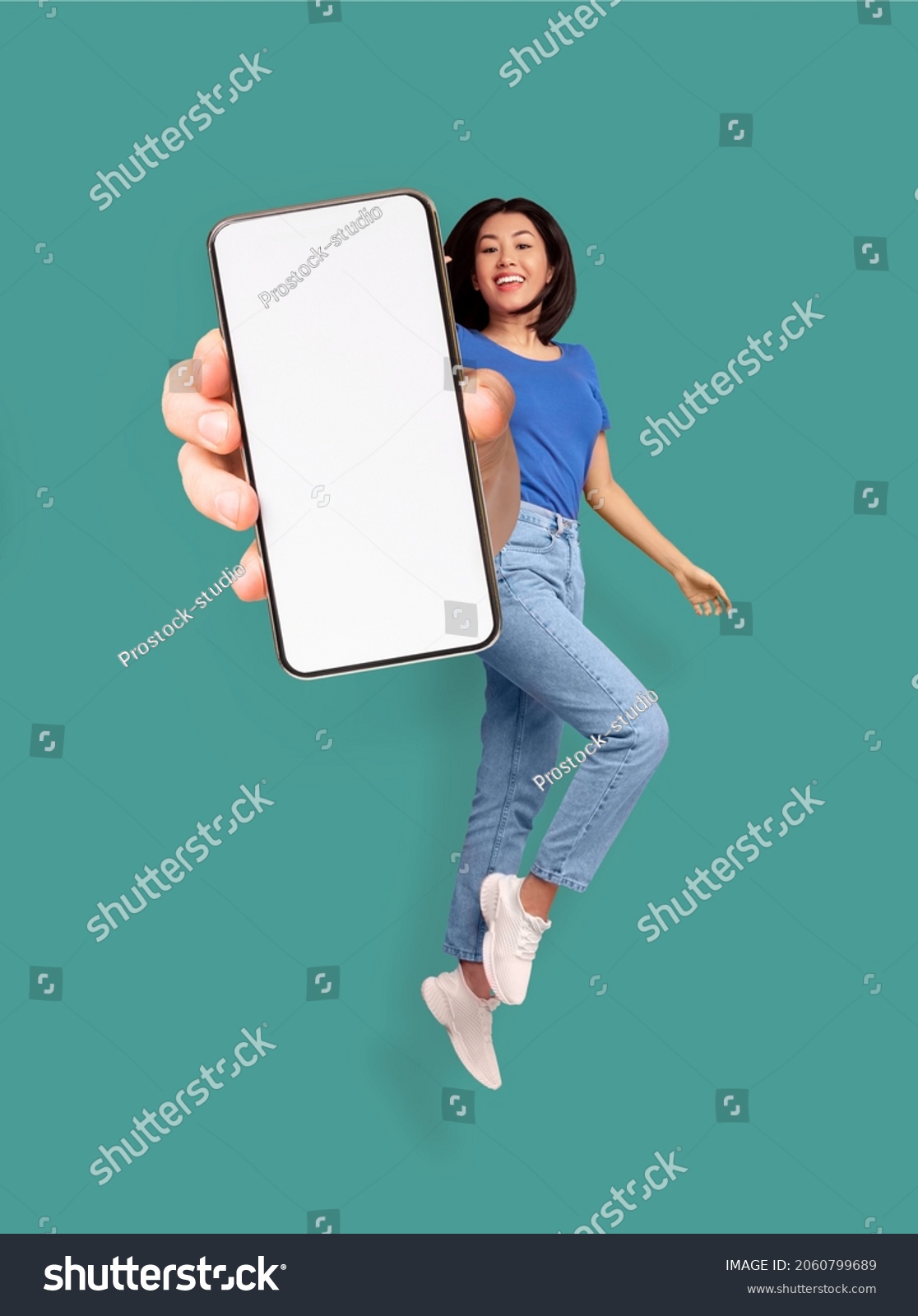 Full length of cheery Asian woman jumping and smiling, showing cellphone with empty space for mobile app or website on screen, turquoise studio background, mockup. Creative collage #2060799689