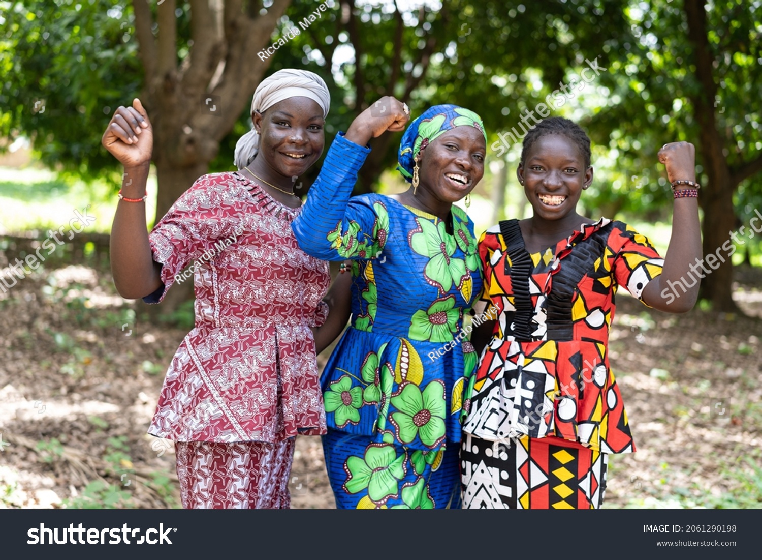 Group of young black African villagers in colourful traditional dresses smiling at the camera with their clenched fists as a symbol for women's strength and gender equality #2061290198