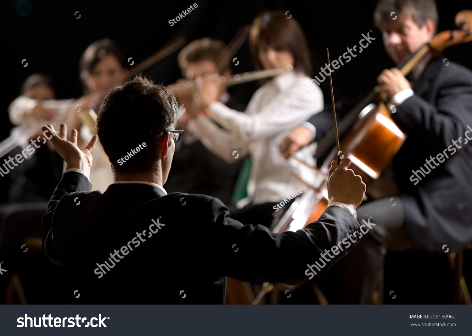 Conductor directing symphony orchestra with performers on background. #206150962