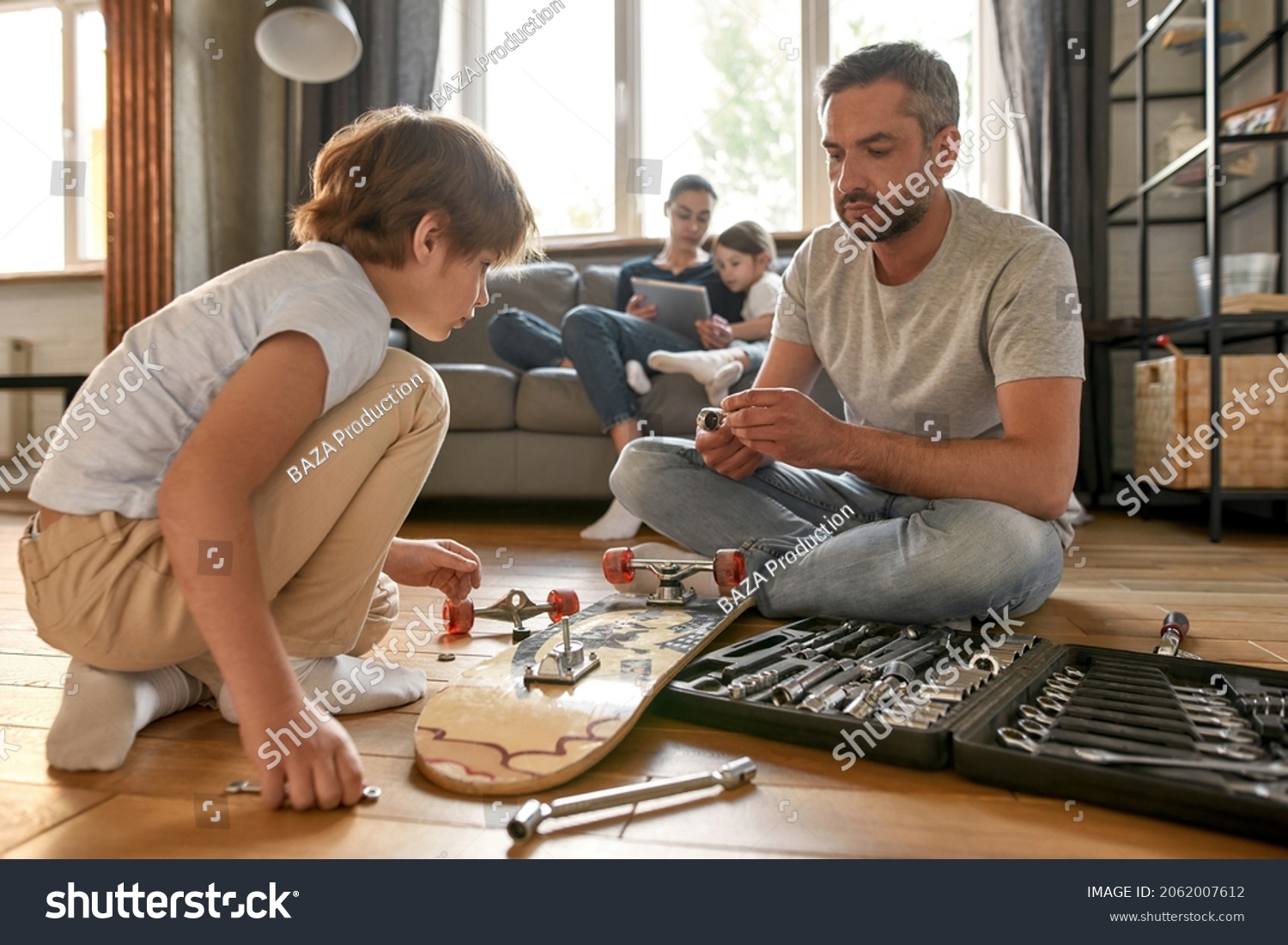 Caucasian dad and teenage son sit on floor at home repair skateboard with toolset in box. Young father teach small teen boy child fixing board with tools equipment. Handyman, fatherhood concept. #2062007612