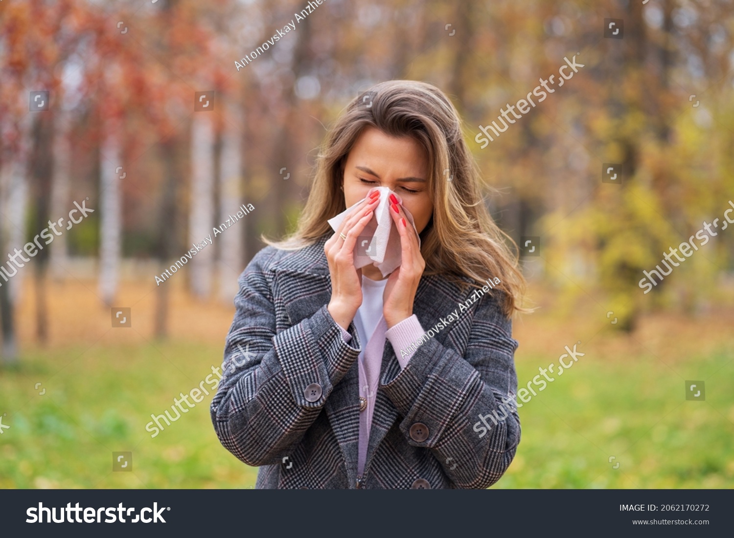 A girl stands on the street in a park in autumn and blows her nose in a handkerchief #2062170272