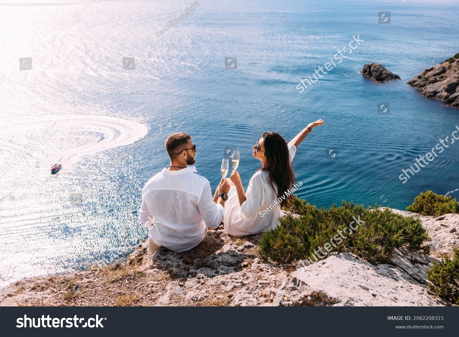 A couple in love celebrates their engagement on the seashore. A beautiful couple drinks champagne by the sea. Honeymoon trip. Lovers on the beach. Wedding travel. Couple on vacation. Copy space #2062208315