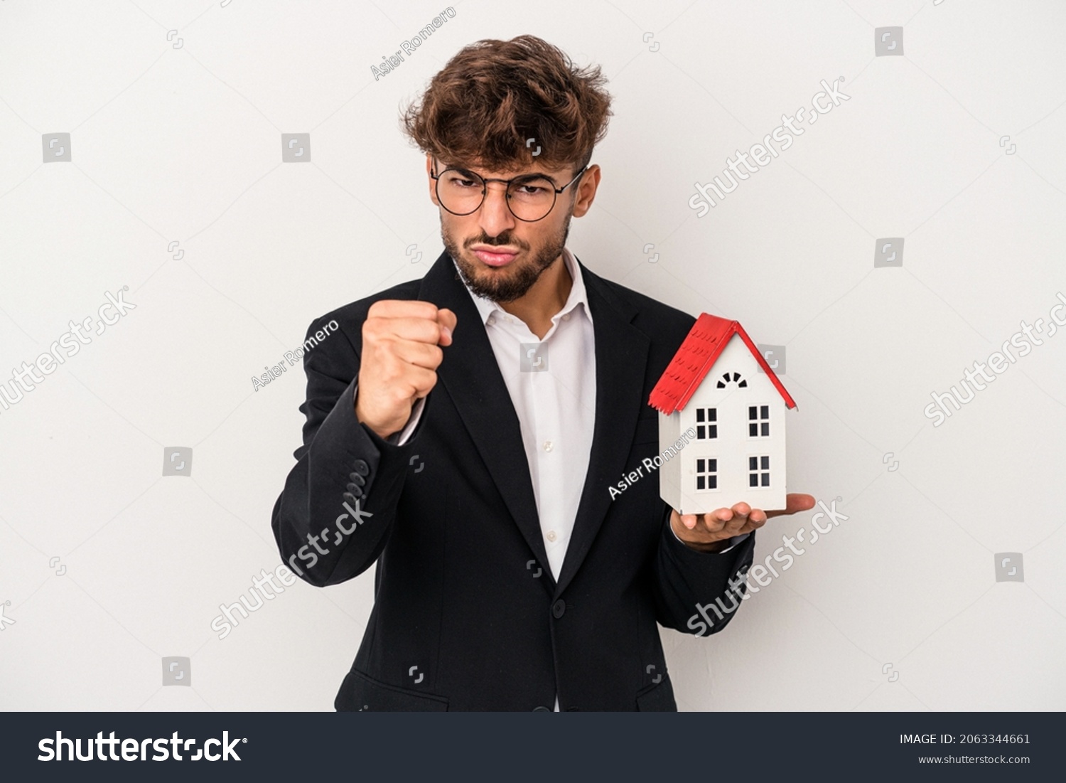 Young arab real estate man holding a model house isolated on isolated background showing fist to camera, aggressive facial expression. #2063344661