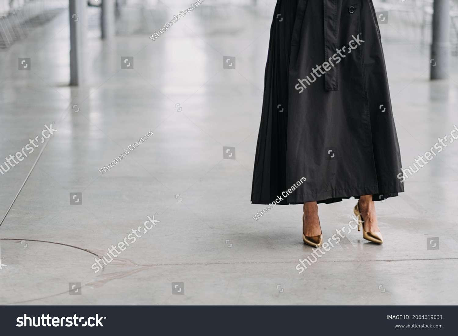 A female in a long black skirt and gold heels in a white room #2064619031